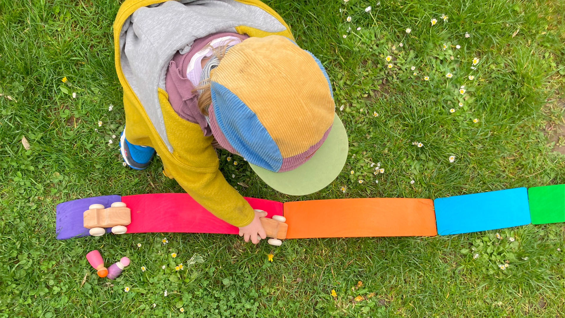 Ein Kind lässt im Gras Holzautos über bunte Holzbretter fahren.