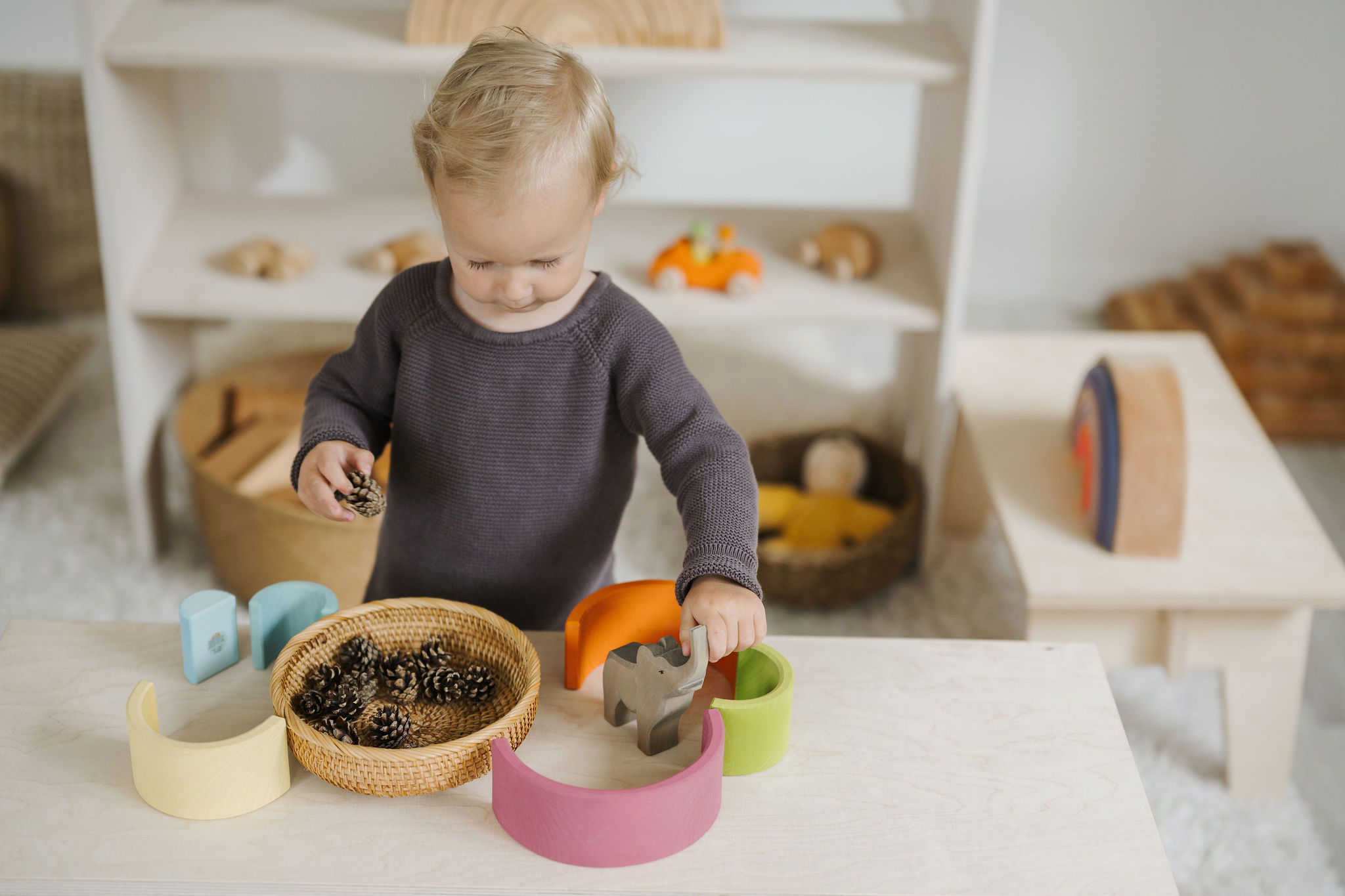 Toddler plays with wooden animals, wooden bows and pine cones