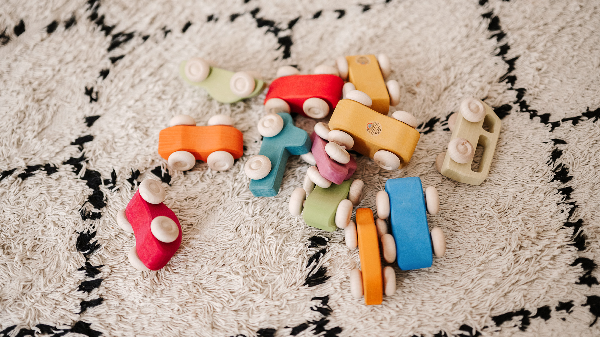 Colourful wooden cars lie on a carpet.